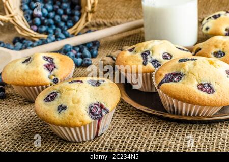 Blueberry Muffins Milch und Marmelade im Hintergrund und Korb voll mit Heidelbeeren Stockfoto