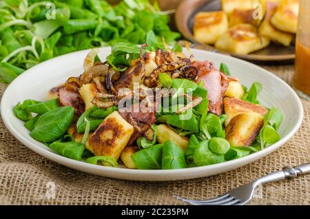 Kartoffel-Gnocchi mit Sommer-Salat, Speck und Röstzwiebeln. Gnocchi gekocht und dann auf Pfanne für Golden knusprig gebraten Stockfoto