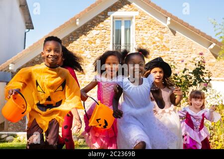 Close Portrait einer Gruppe von Kindern laufen im Halloween Kostüm auf dem Rasen vor dem Haus zusammen, schreien mit Süßigkeiten Eimer Stockfoto