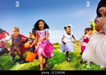 Große Gruppe kleiner Kinder laufen im Halloween Kostüm auf dem Rasen mit Eimern für Süßigkeiten Stockfoto