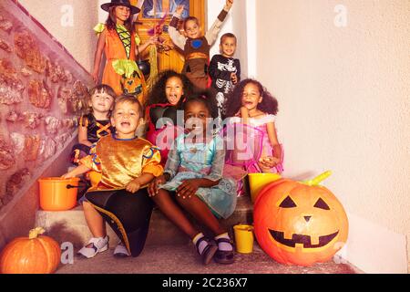 Große Gruppe von Halloween-Kinder in Kostümen sitzen auf der Treppe mit orangefarbenen Kürbis und Eimer lächeln Blick auf die Kamera Stockfoto