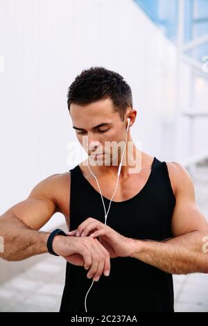 Junge zuversichtlich Sportler bei smart Uhren suchen, Kontrolle ein Cardio nach dem Training, das Hören von Musik im Kopfhörer. Außerhalb. Sport Konzept. Stockfoto