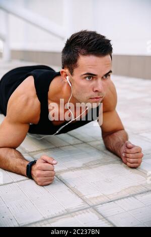 Nahaufnahme der Junge muskulöse Sportler der Ohrhörer, Push-ups an Ellbogen, heraus zu arbeiten. Sport und gesunde Lebensweise. Stockfoto