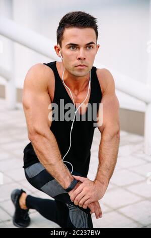 Junge muskulöse Athleten in der Ohrhörer, körperliche Übungen für Körper, während Sie im Freien arbeiten, mit schwarzen Sportswear. Stockfoto