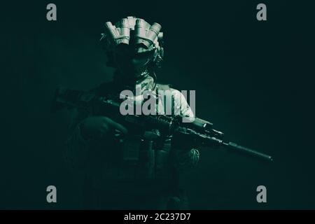 Halbe Länge, Low Key studio Shoot der Armee Soldat, marine Infanterist in Maske, camo Uniform, ausgestattete moderne Munition, bewaffneten Dienst Gewehr stehend Stockfoto