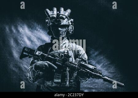 Halbe Länge, Low Key studio Shoot der Armee Soldat, marine Infanterist in Maske, camo Uniform, ausgestattete moderne Munition, bewaffneten Dienst Gewehr stehend Stockfoto