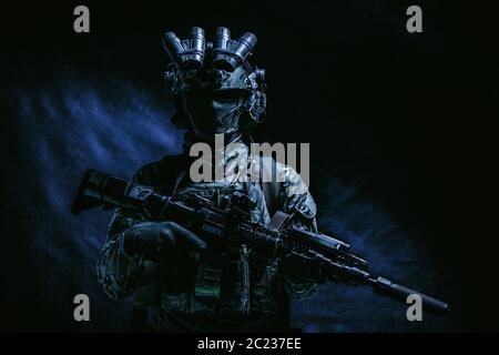 Halbe Länge, Low Key studio Shoot der Armee Soldat, marine Infanterist in Maske, camo Uniform, ausgestattete moderne Munition, bewaffneten Dienst Gewehr stehend Stockfoto