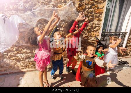 Gruppe von Kindern heben die Hände in die Luft und greifen nach Süßigkeiten, die Halloween Kostüme tragen, die an der Wand stehen und einen Geist darauf haben Stockfoto