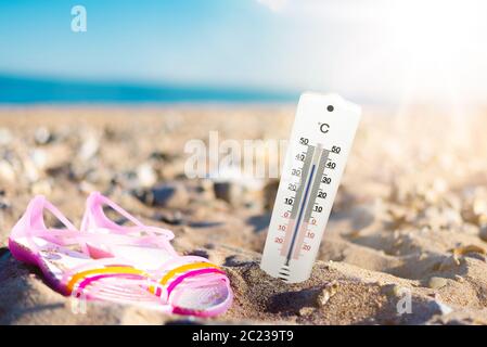 Sommerwetter und Hörkonzept, Thermometer im Sand am Strand gegen Meer und blauen Himmel Stockfoto