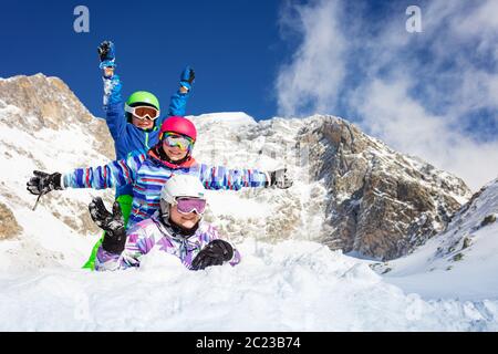 Haufen Kinder, eine auf der anderen lag im Schnee über dem blauen Himmel in den Bergen und heben die Hände Stockfoto