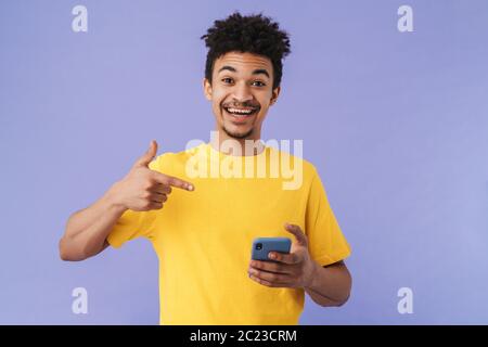 Foto von lustigen afroamerikanischen Mann zeigt Finger auf Smartphone isoliert über lila Hintergrund Stockfoto
