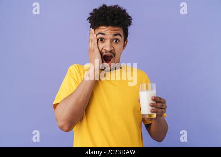 Foto von schockierten afroamerikanischen Mann hält Glas mit Milch isoliert über lila Hintergrund Stockfoto