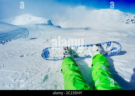 Nahaufnahme des Snowboards an den Beinen über der Bergspitze auf Ski-Resort-Piste mit Höhenwolken bedeckt befestigt Stockfoto