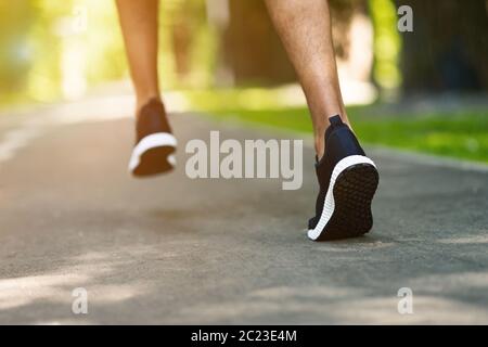 Unerkennbarer schwarzer Kerl in Sportschuhen Joggen im Stadtpark am sonnigen Morgen, Nahaufnahme Stockfoto