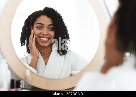 Happy Black Frau Berührt Ihr Schönes Gesicht Beim Blick In Den Spiegel Stockfoto