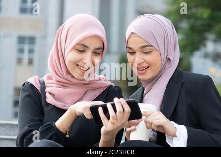 Muslimische Frauen mit Smart Phone, Teilen und Lachen. Stockfoto
