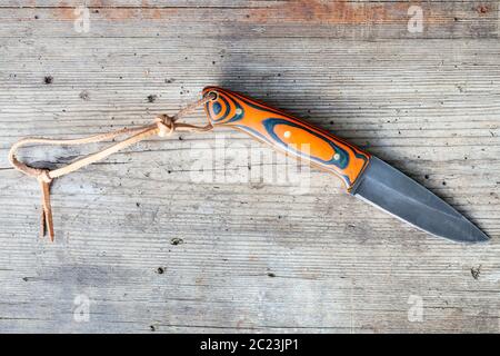 Blick von oben auf die handgefertigte geschwärztem Stahl Messer mit hausgemachten Epoxid- und orange Stoff Griff mit Lederband auf alten Holz- Board Stockfoto