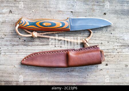 Blick von oben auf die handgefertigte geschwärztem Stahl Messer mit hausgemachten Epoxid- und orange Stoff Griff mit der Hand - lederscheide auf alten Holzplatte genäht Stockfoto