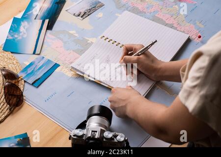 Nahaufnahme einer nicht erkennbaren Frau, die Informationen über die Reise in Notizblock hinzufügt, während Sie Urlaub mit Karte planen Stockfoto
