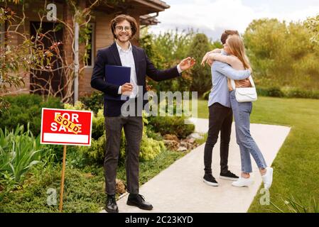 Lächelnder Manager und umarmt Millennial Paar in der Nähe von schönen Haus im Freien Stockfoto