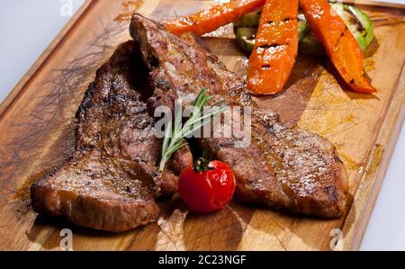 Schwarzes Angus Steak auf einem Holzbrett gegrillt und mit Gemüse garniert Stockfoto