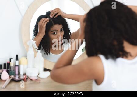 Schuppen-Problem. Traurige Schwarze Frau, Die Ihre Haarwurzeln Im Spiegel Betrachtet Stockfoto