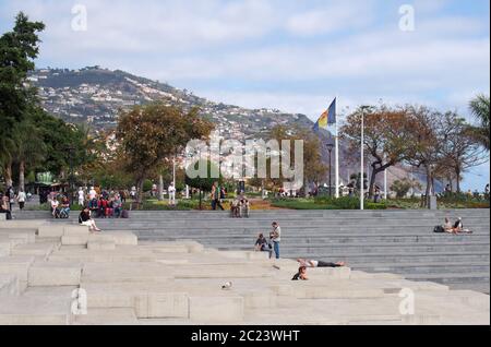 Die Uferzone des hafens von funchal mit Menschen saß auf den Betontreppen vor der Strandpromenade und dem öffentlichen Park mit Blick o Stockfoto