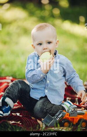 Portrait von wenig elegante blonde Junge unter Gras und mit Apfel. Stockfoto