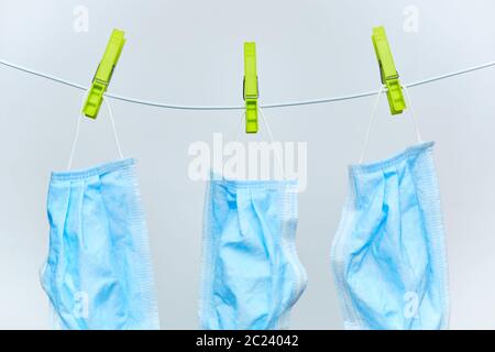 Gebrauchte Einweg-Schutz chirurgische Masken Trocknen auf einer Wäscheleine mit grünen Wäscheklammern auf weißem Hintergrund. Stockfoto