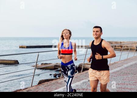 Sportlicher junger Mann und Frau in Sportkleidung jogging zusammen auf dem Kai in der Nähe des Meeres. Training am Kai. Stockfoto