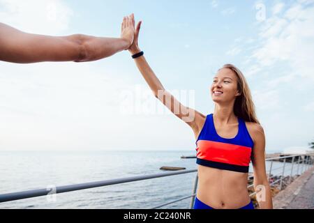 Lächelnd schöne Fitness Mädchen ihren Freund eine hohe fünf, stehend auf die Quay in der Nähe des Meeres. Sport Konzept. Stockfoto