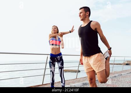 Attraktive fröhlicher junger Paare tun Stretching Übungen für Körper, während Sie arbeiten am Kai, in der Nähe des Meeres. Gesunde Lebensweise. Stockfoto