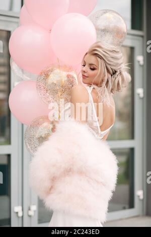 Atemberaubende blonde Frau in geschnürte Top oder Kleid und rosa Fell mit Luftballons. Stockfoto