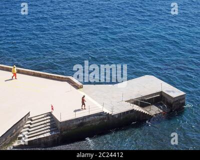 Luftaufnahme eines Mannes, der sich vorbereitet, vom Betonpier in funchal madeira zu schwimmen, mit einem Rettungsschwimmer in Uniform, der die Gegend patrouilliert Stockfoto