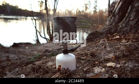 Nahaufnahme eines Gasbrenners, auf dem ein Wasserkocher mit Deckel steht, kocht Wasser, Dampf, Kochen im Freien. Es kocht Nahrung. Stockfoto