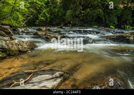 Stromabwärts von einem Wasserfall Wildwasser, das sich schnell durch die Felsen und Felsbrocken des Flusses mit dem Wald im Hintergrund auf einem hellen sonnigen bewegt Stockfoto