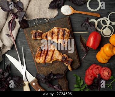 Saftig gegrilltem Schweinefleisch Steaks auf einem braunen Brett, frische rote und gelbe Tomaten Stockfoto