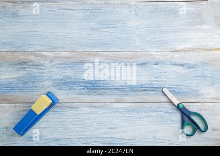 Schere und Hefter auf einem blauen und weißen schäbig vintage Holz- Hintergrund. Die Aussicht von oben. Flach Stockfoto