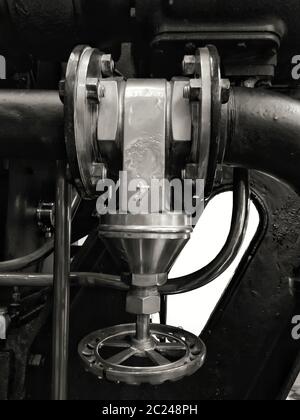 Ein großes altes Industrieventil aus Metall mit rundem Griff, montiert auf einer großen schwarzen Maschine mit Schrauben und glänzenden Rohren Stockfoto