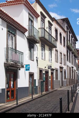 Eine schmale gepflasterte Straße in funchal mit typischen, weiß bemalten Geschäften und Häusern mit Balkonen und einem hellen, sonnendurchfluteten Himmel Stockfoto