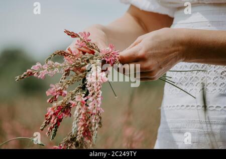 Nahaufnahme der Hände einer Frau, die wilde Blumen in eine Blumenkrone umflechten Stockfoto