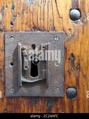 Ein großes quadratisches rostiges Eisenschloss mit Schlüsselloch in einer alten lackierten Holztür mit dem Ende des Schlüssels sichtbar und Metallnieten Stockfoto