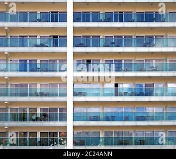Vollformat-Bild eines großen Wohnkomplexes mit geometrischen Reihen von sich wiederholenden Fenstern und Balkonen mit Außenmöbeln Stockfoto
