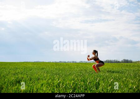 Mädchen Athlet tut Kniebeugen in der Natur, Übungen für das Gesäß. Junge Frau gehen in für Sport, gesunde Lebensweise, athletischen Körper. Sie ist in Sportbekleidung, Stockfoto