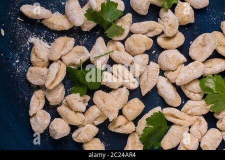 Einige roh hergestellte Gnocchi mit Basilikum auf einem blauen Tisch Stockfoto