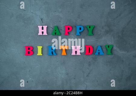 Die bunten happy birthday Wort ist aus Holz Buchstaben auf einem grau verputzte Wand Hintergrund gemacht Stockfoto