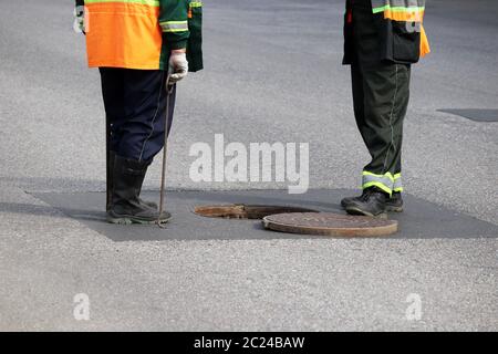 Arbeiter über der offenen Kanalluke auf einer Straße. Konzept der Reparatur von Abwasser, unterirdische Versorgungseinrichtungen, Wasserversorgung, Kabelverlegung Stockfoto