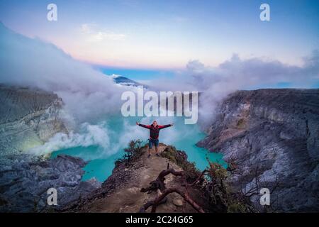 Mann Reisende am Rande des Kraters mit bunten Himmel am Morgen stehen. Schöner Ijen Vulkan mit saurem See und Schwefelgas aus Krater, Indonesien Stockfoto