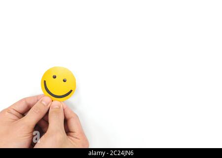 Glück und Positivität Konzept. Hand hält gelb lächelndes Gesicht in weißem Hintergrund mit Kopierraum. Stockfoto