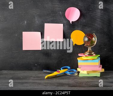 Stapel von mehrfarbigen klebrigen Aufkleber, Glaskugel, Schere auf schwarzem Holz- Hintergrund, Konzept Zurück zur Schule Stockfoto